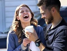 a man and woman laughing while holding coffee cups