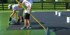 two men are painting the roof of a building with green paint and yellow plastic buckets