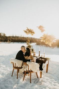 a man and woman sitting at a table in the snow with candles on top of it