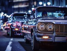 several classic cars are parked on the street at night