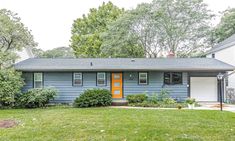 an image of a blue house with orange door in the front yard and green grass