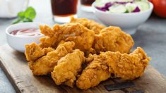 fried chicken on a wooden cutting board with dipping sauces and salad in the background