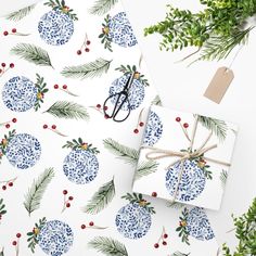 wrapping paper with blue and white christmas ornaments on it next to evergreen branches, pine cones and scissors