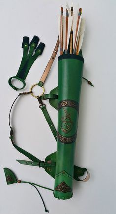 a green leather case with arrows and other items around it on a white table top