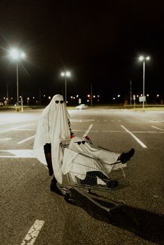 a person dressed as a ghost pushing a shopping cart in an empty parking lot at night