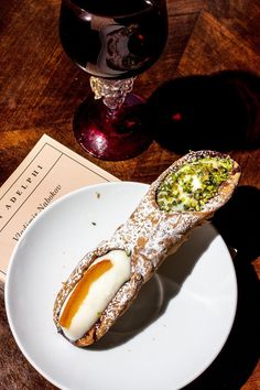 a white plate topped with a pastry next to a glass of wine on a wooden table