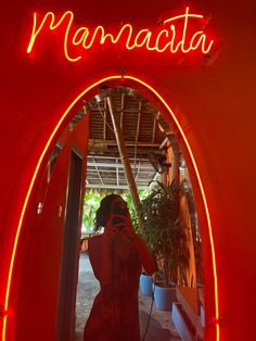 a woman standing in front of a red neon sign with the word manabata on it