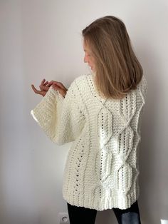 a woman standing in front of a wall wearing a white sweater and black leggings