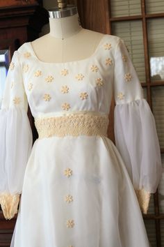 a white dress with yellow flowers on the waist and long sleeves, sitting on a mannequin