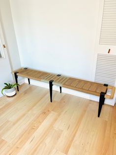 a wooden bench sitting on top of a hard wood floor next to a white wall