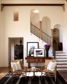 a living room filled with furniture next to a stair case and wooden table on top of a hard wood floor