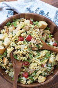 a wooden bowl filled with pasta salad on top of a table next to a napkin