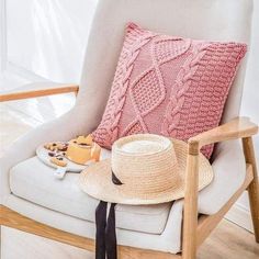 a white chair with a pink knitted pillow and a hat on top of it