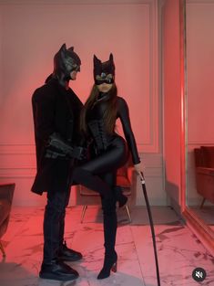 two people dressed up as batman and catwoman standing in a room with red lighting