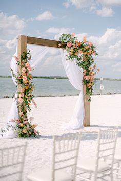 an outdoor wedding setup on the beach with white chairs and flowers in the archways