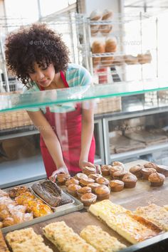 a woman in an apron looking at pastries on display behind a glass counter - stock photo - images