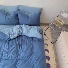 a bed with blue sheets and pillows on top of it next to a white dresser