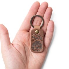 a hand holding a brown leather keychain with a camper and mountains on it