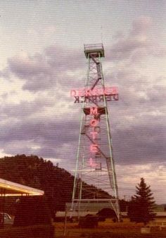 a large neon sign sitting on the side of a tall metal tower next to a parking lot