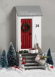 a small white house with a red door and wreath on it's front porch