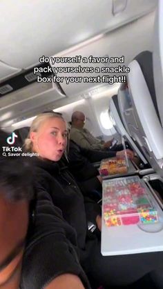 two people are sitting on an airplane and one person is looking at the camera