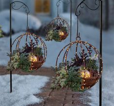 three metal ornaments with lights and plants in them on snow covered ground next to building