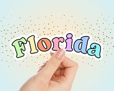 the word florida written in multicolored letters is held up by a person's hand