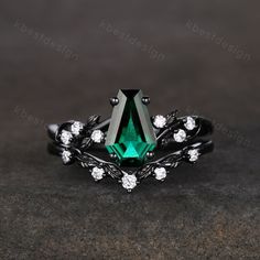 an emerald colored stone surrounded by white diamonds on top of a black metal band ring