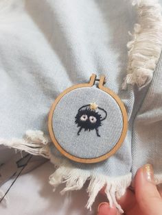 someone is stitching an embroidered black sheep on a light blue shirt with fringes