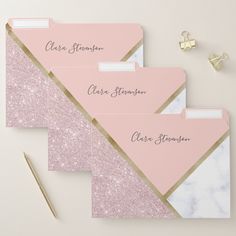 three pink and white envelopes with gold trim on them, next to a pair of scissors