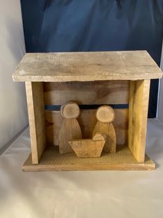 a wooden box with two people in it and a blue background behind the box is a white sheet