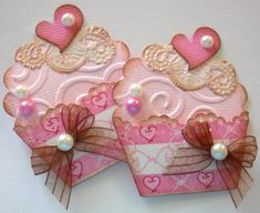 two pink heart shaped boxes with bows and pearls on them, sitting side by side