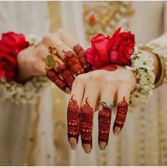 two hands with henna tattoos and red flowers on their fingers, both holding onto each other