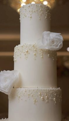 a three tiered white wedding cake with pearls and roses on it's side