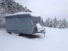 a covered trailer parked in the snow next to some pine trees and evergreens on a cloudy day