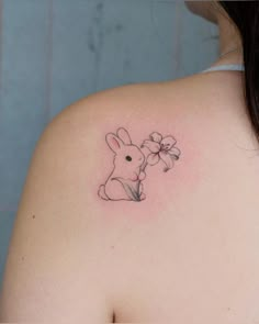 a woman's back shoulder with a small tattoo of a bunny holding a flower