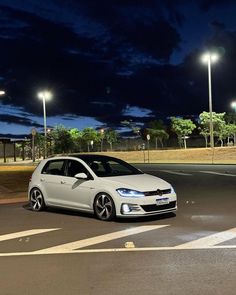 a white car parked on the side of a road next to a parking lot at night