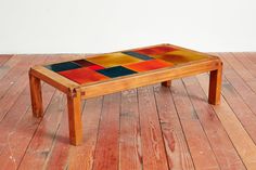 a wooden table with multicolored tiles on it's top sitting on a wood floor