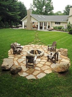 a stone fire pit in the middle of a yard with chairs and tables around it