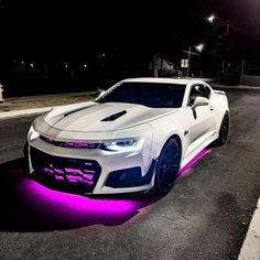 a white chevrolet camaro with purple lights on it's hood and front bumper