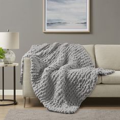 a living room with a white couch and gray blanket on the floor next to a lamp