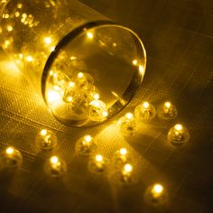 a glass jar filled with yellow lights on top of a table next to some white balls