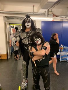 two people dressed as kiss band members posing for a photo in an office building with other people behind them