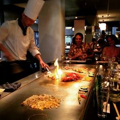 a chef is preparing food on a grill with people sitting at the bar behind him