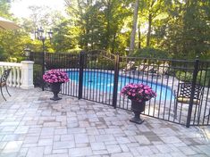 two flower pots sitting in front of a fence next to a swimming pool with flowers on it