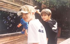 two young boys standing next to each other with bubbles in the air and water behind them