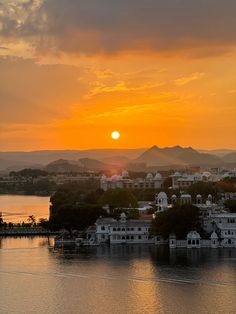 the sun is setting over an island with houses on it and mountains in the background