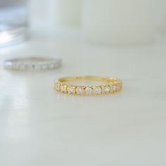 two gold and diamond wedding bands on a white countertop next to an empty candle