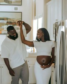 a pregnant woman standing next to a man in a kitchen