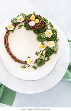 a cake decorated with flowers and birds nest on top of a white platter next to green napkins